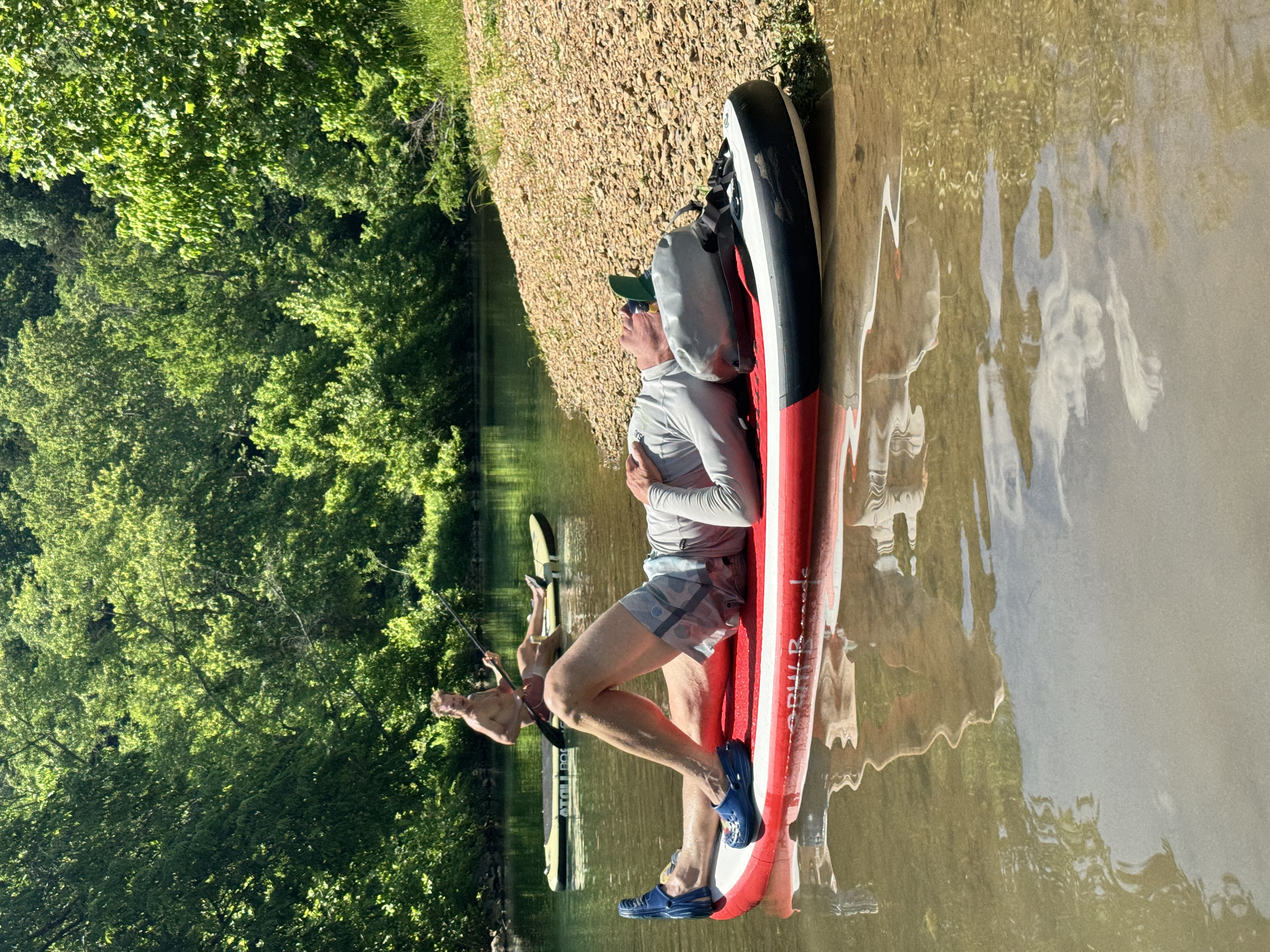 A paddler relaxing on the shore of Little Sugar Creek with a SUP board