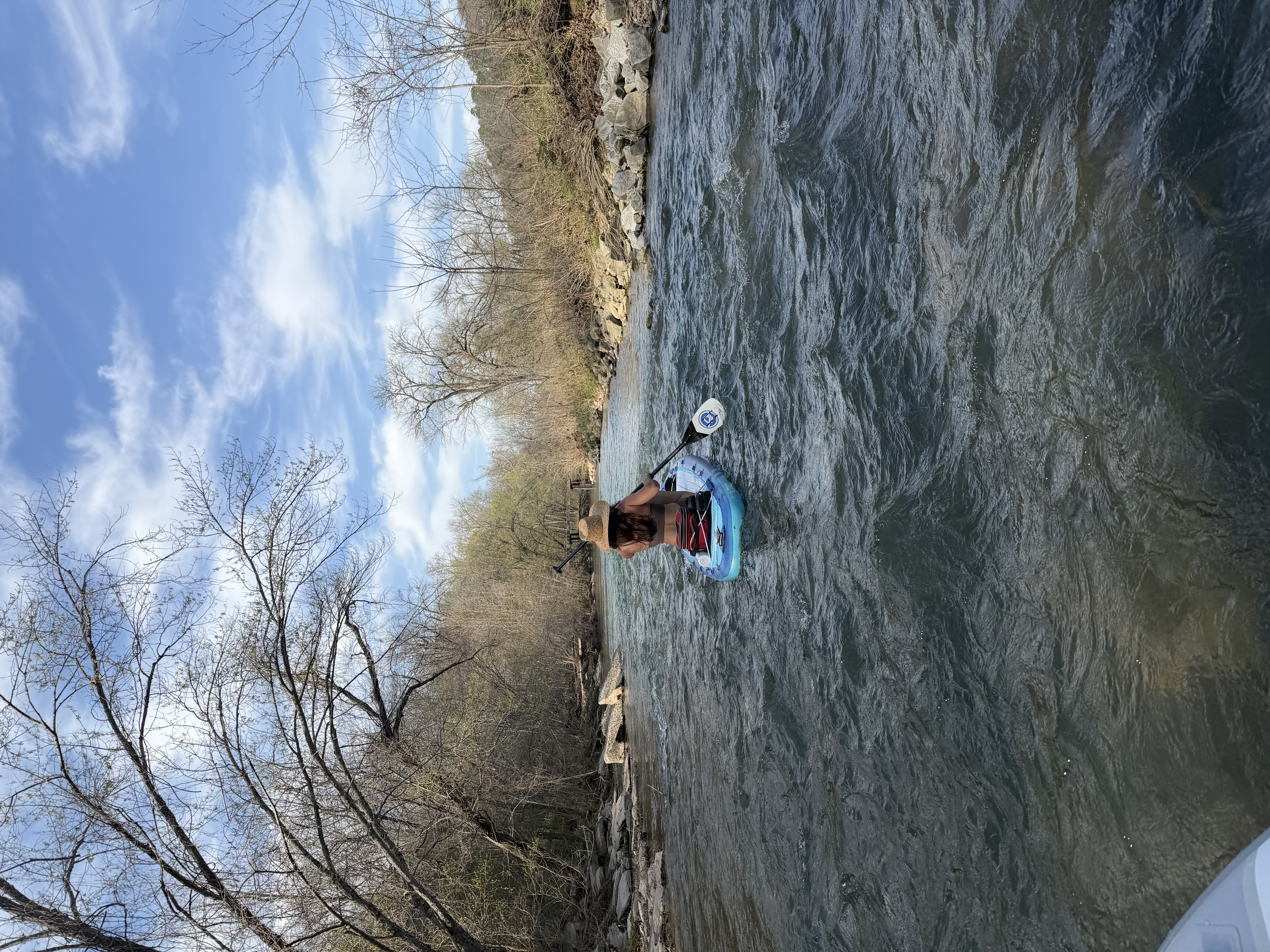 A paddler sitting on a SUP board through a shallow section of Little Sugar Creek