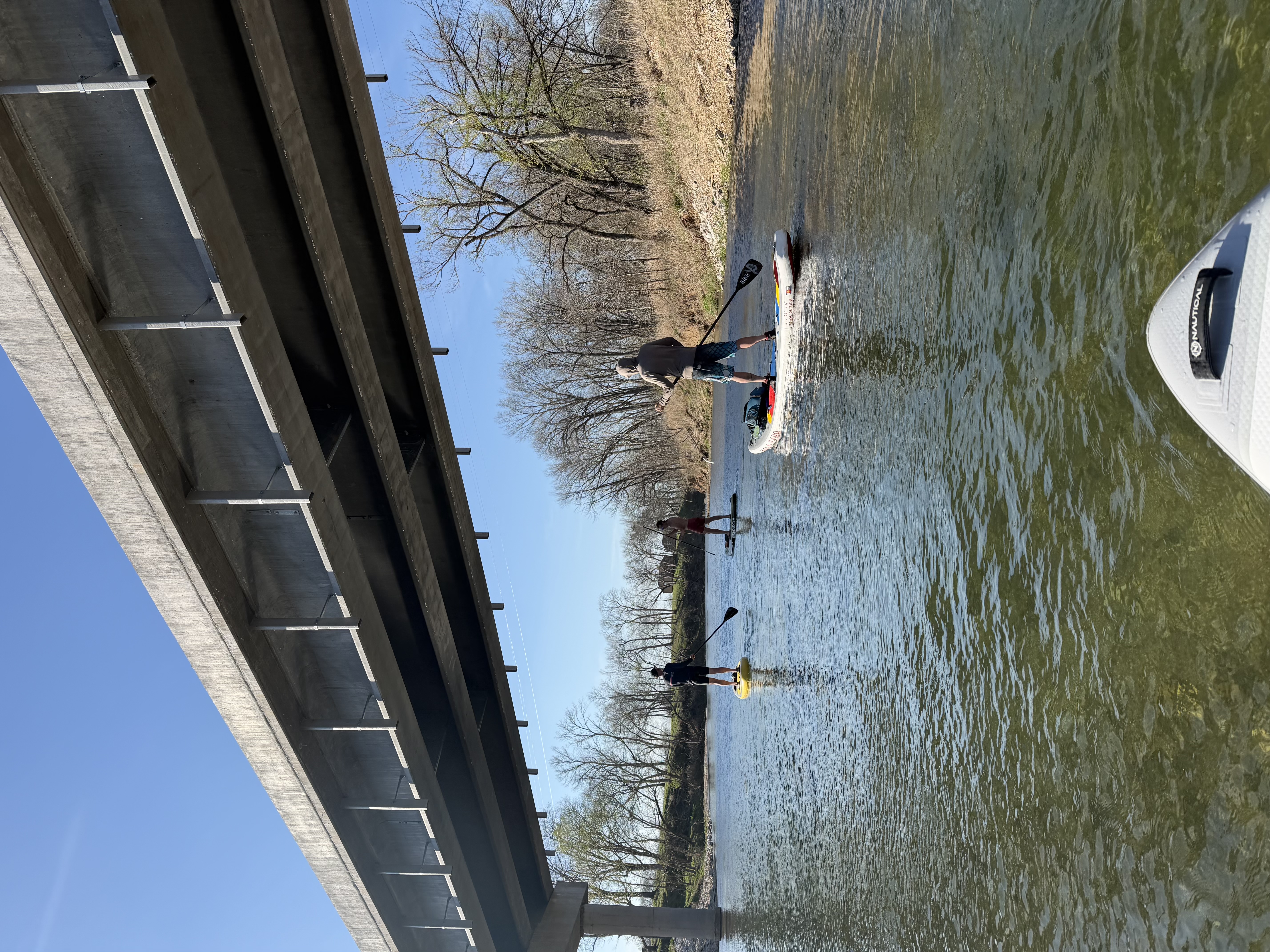 A paddler standing on a SUP board floating under a bridge on Little Sugar Creek